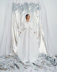 An unconventional pastel white gown with a wide, floaty trench and bow sleeves, designed for the avant-garde bride. A sustainable wedding collection designed in Vienna, that redefines modern bridal fashion with its striking, minimalist aesthetic.